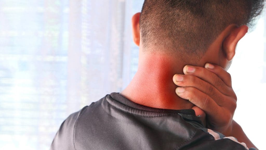 guy holding his hand to his neck that is highlighted red to signify neck pain